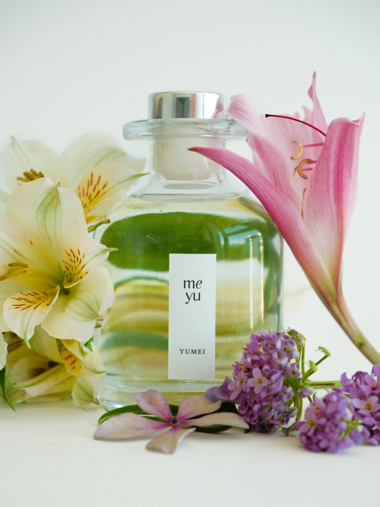 Yumei reed diffuser surrounded by flowers on white background - gentle floral home fragrance by Meyu Vancouver